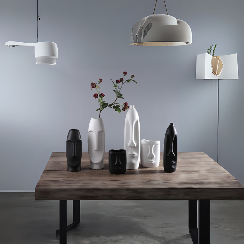 Minimalist table with black and white abstract face vases under modern pendant lights.
