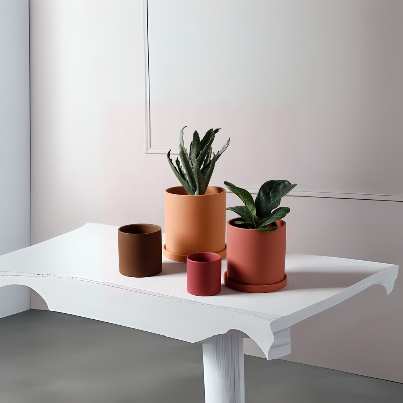 Set of four ceramic plant pots in earthy tones, two with green plants and two empty.